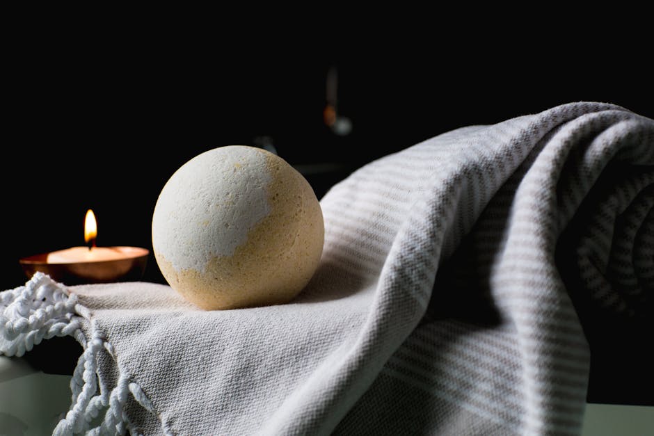 Elegant spa setup featuring a lit candle and a bath bomb on a soft towel, perfect for relaxation.
